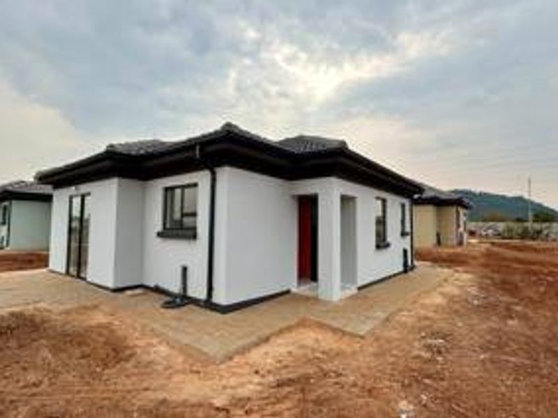 A modern single-story residential house featuring a tiled roof, white exterior walls, and aluminium window frames, situated on an undeveloped plot.