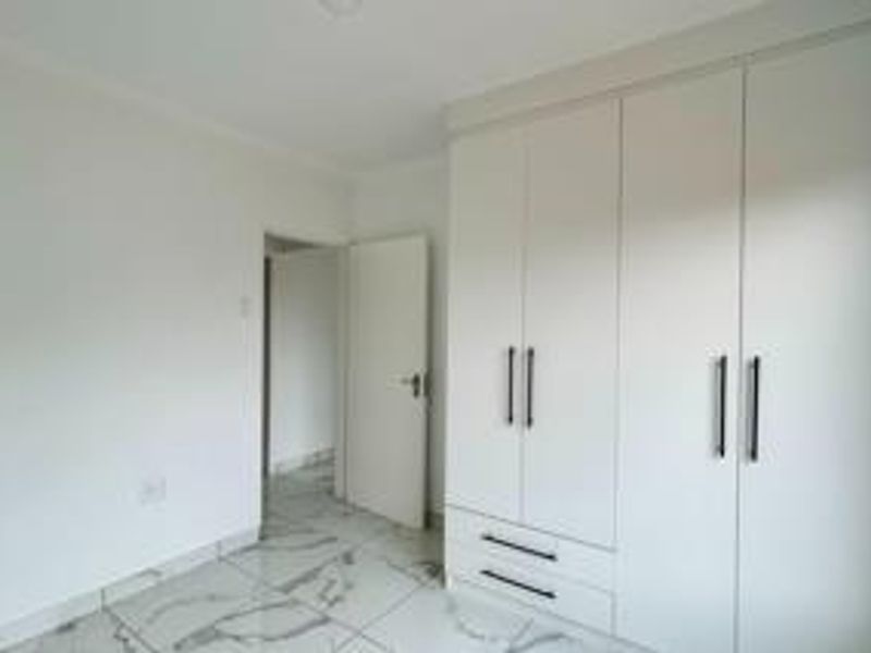 A bright, empty bedroom featuring modern white built-in wardrobes and polished marble-look floor tiles.