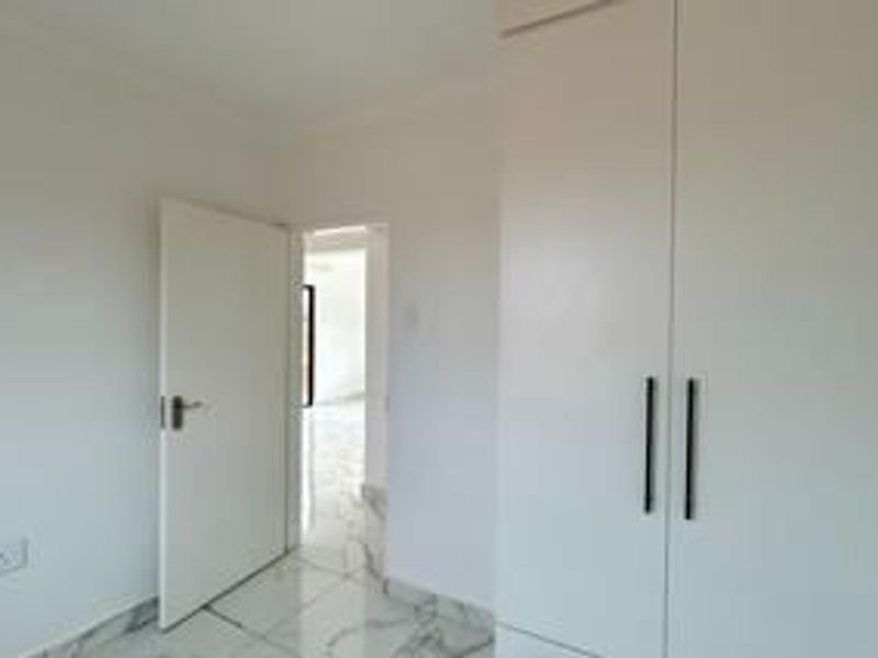 A clean, empty bedroom featuring modern white built-in cupboards and light-colored tiled flooring with a marble-effect finish.