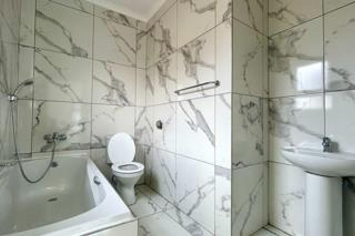 A modern bathroom featuring floor-to-ceiling marble-look wall tiles, a bathtub with shower mixer, a pedestal sink, and a toilet.