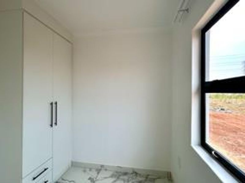 A bright, modern bedroom featuring built-in wardrobes, marble-look tiled flooring, and a large window with views of the surrounding area.