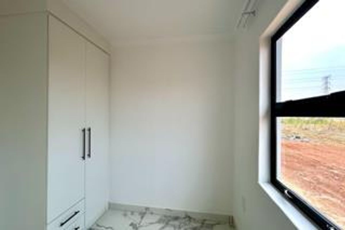A bright, modern bedroom featuring built-in wardrobes, marble-look tiled flooring, and a large window with views of the surrounding area.