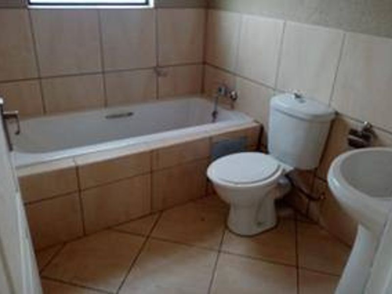 A functional bathroom featuring a built-in bathtub, pedestal basin, and toilet with neutral ceramic tiling throughout.