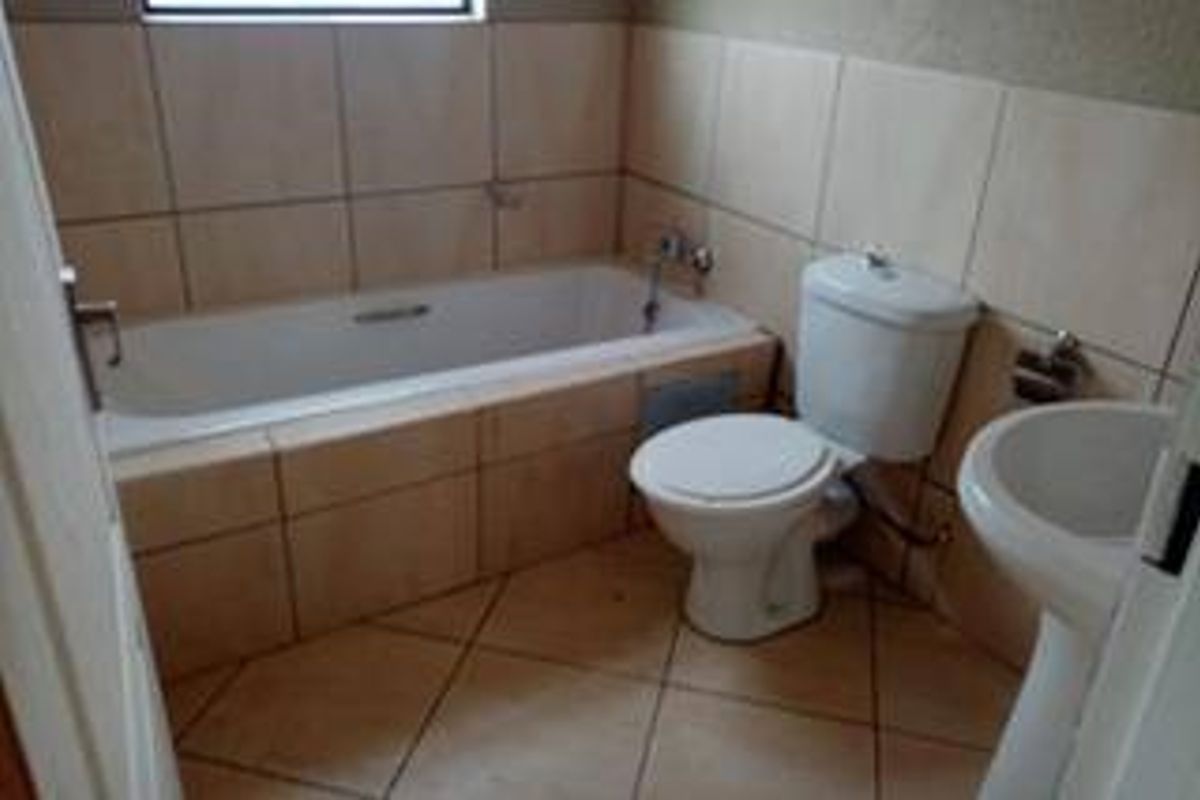 A functional bathroom featuring a built-in bathtub, pedestal basin, and toilet with neutral ceramic tiling throughout.