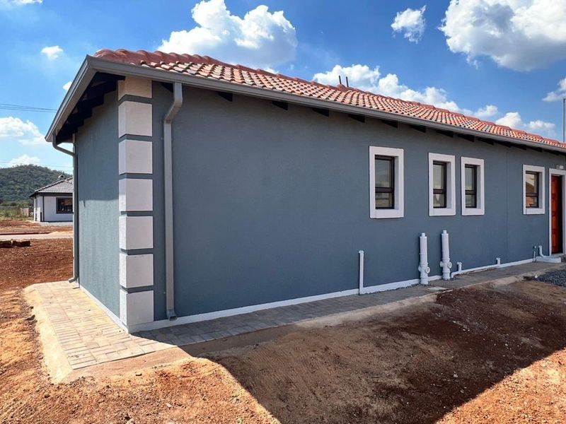 Rear view of a modern single-story house featuring grey rendered walls with white quoins, a tiled roof, and paved perimeter walkway.