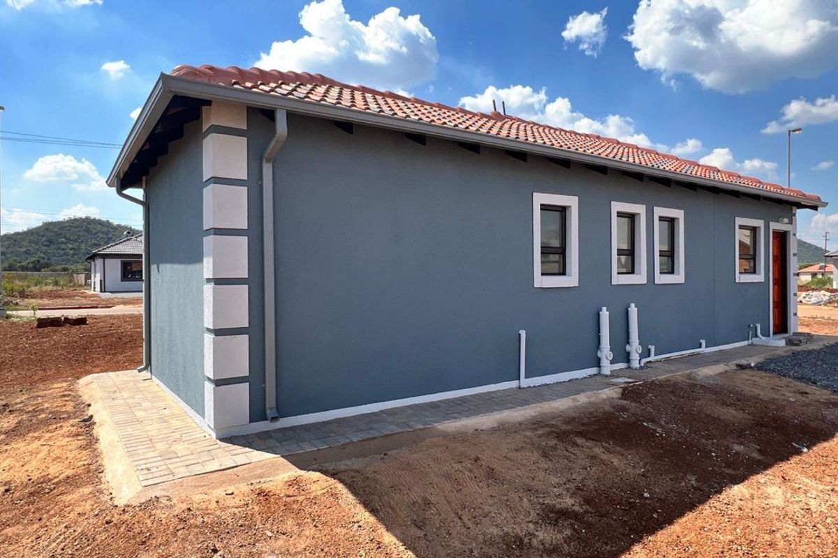 Rear view of a modern single-story house featuring grey rendered walls with white quoins, a tiled roof, and paved perimeter walkway.