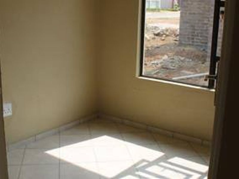 A compact, empty bedroom featuring tiled flooring and a large window, providing a blank canvas for interior design and furnishing.