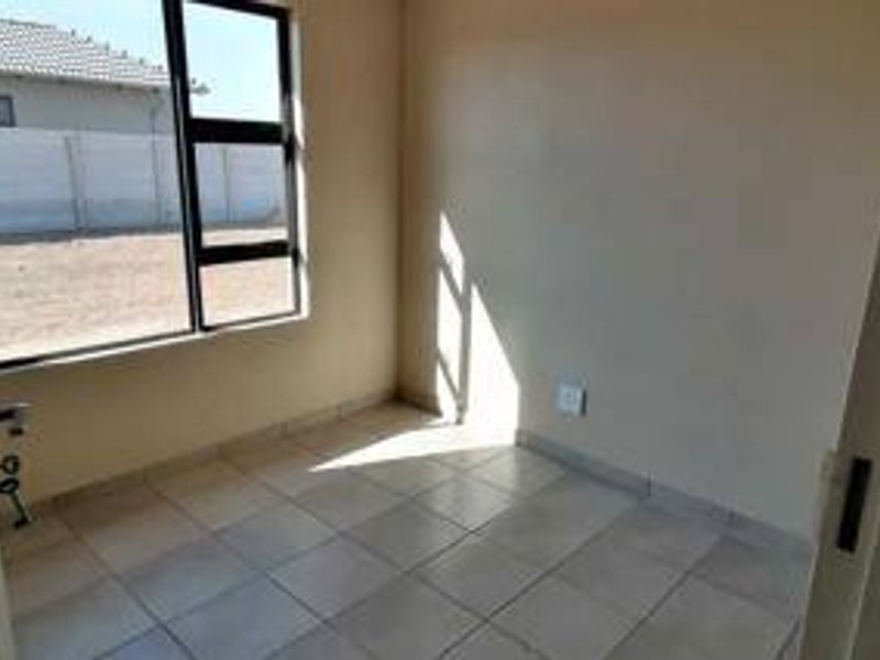 A vacant bedroom featuring neutral tiled flooring and a large aluminium-framed window, offering a clean and blank canvas for personalization.