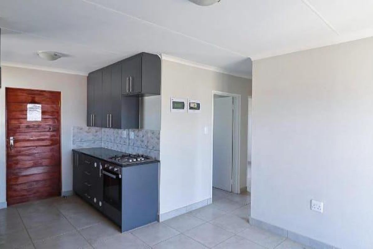 A compact, modern kitchen featuring dark grey cabinetry, a built-in gas hob, an oven, and neutral tiled flooring in an open-plan layout.