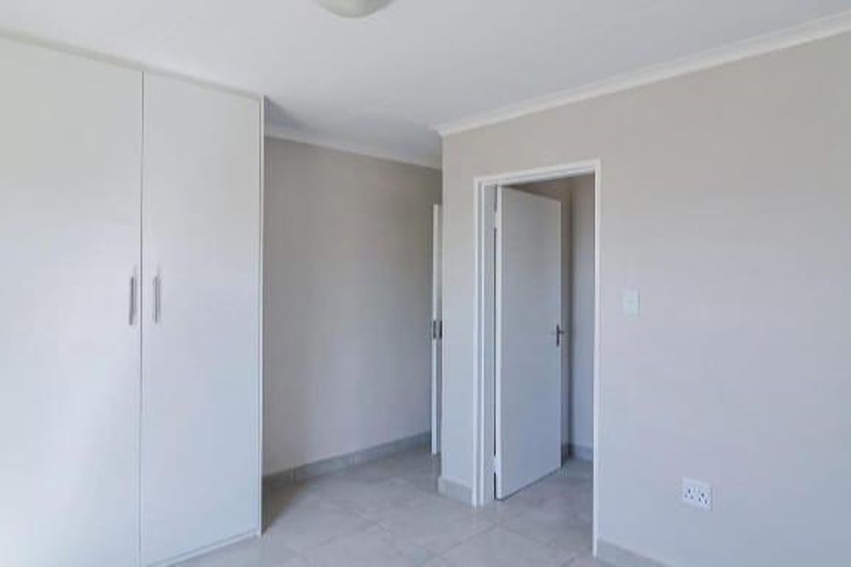 A clean, empty bedroom featuring neutral walls, tiled flooring, and ample built-in cupboard storage.
