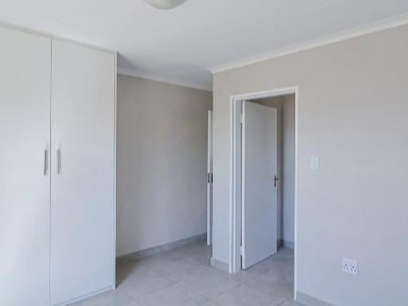 A clean, empty bedroom featuring neutral walls, tiled flooring, and ample built-in cupboard storage.