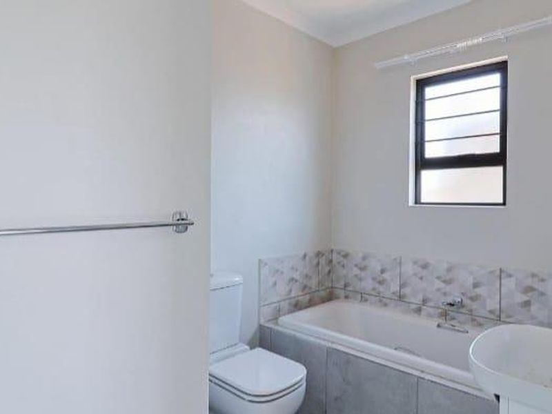 A clean and functional bathroom featuring a bathtub, toilet, basin, and modern tiled splashback with a window for natural light.