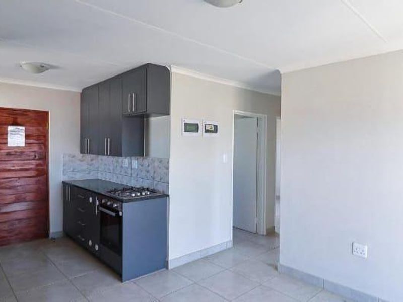 A compact, modern kitchen featuring dark grey cabinetry, a built-in gas hob, an oven, and neutral tiled flooring in an open-plan layout.
