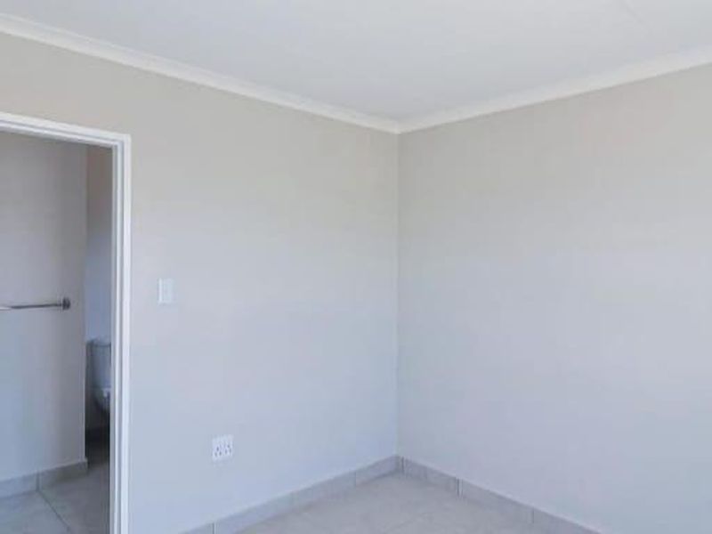 A clean, neutral-toned bedroom featuring tiled flooring and a coved ceiling, with an adjoining bathroom area visible through the doorway.