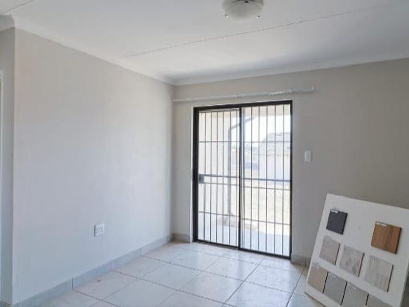 A bright, empty living room featuring neutral walls, tiled flooring, and a sliding glass door with a security gate leading to the exterior.