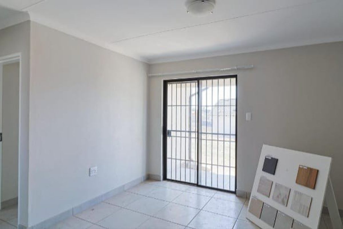 A bright, empty living room featuring neutral walls, tiled flooring, and a sliding glass door with a security gate leading to the exterior.