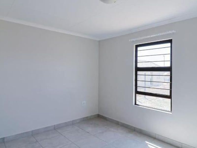 A clean, empty bedroom featuring neutral tiled flooring, white walls, and a window fitted with security bars.