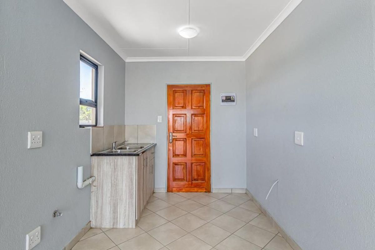 A clean and functional laundry room featuring tiled flooring, built-in sink with cabinetry, and a solid timber door.