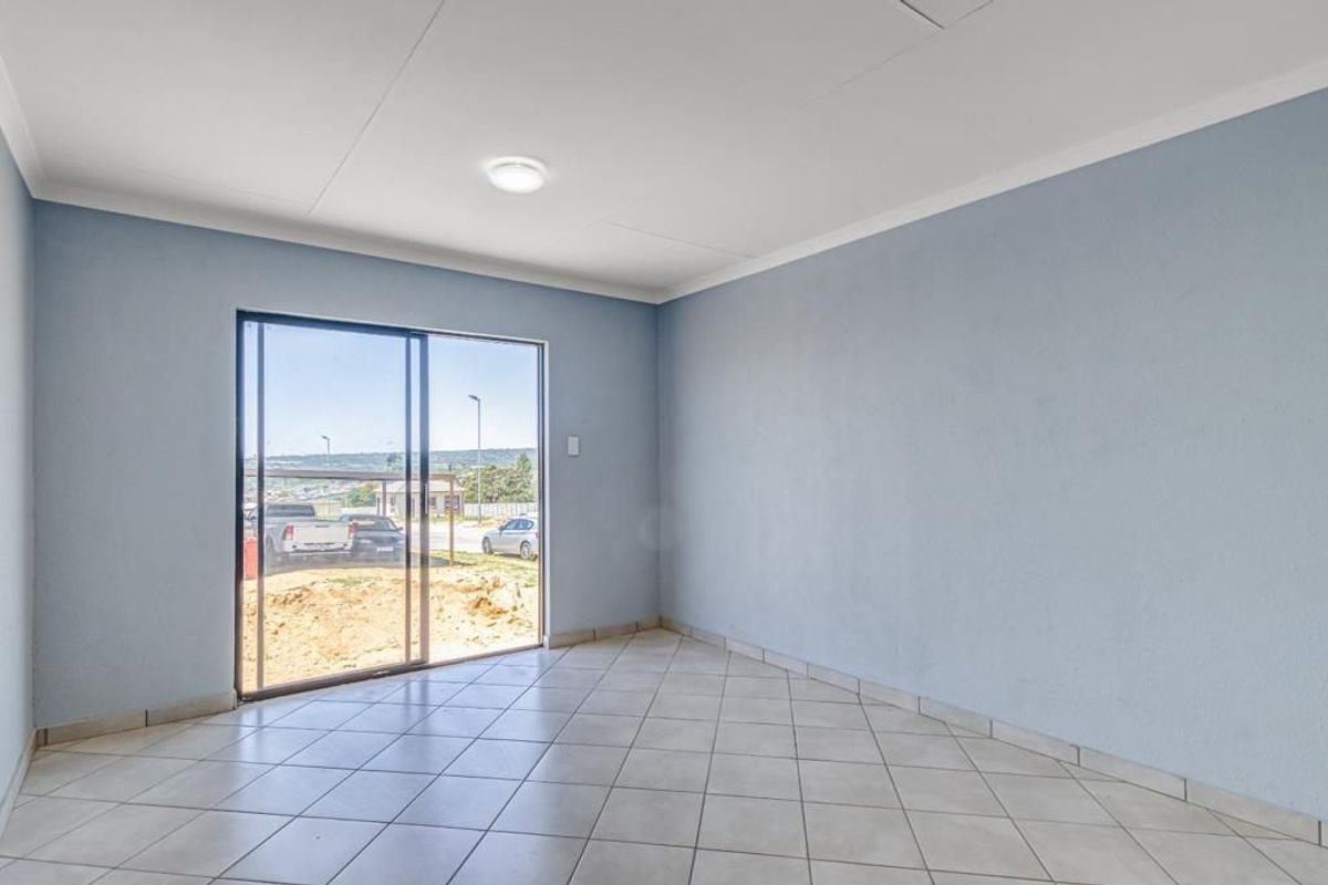 A bright, empty living room featuring neutral ceramic floor tiles, coved ceilings, and a sliding glass door providing access to the exterior.
