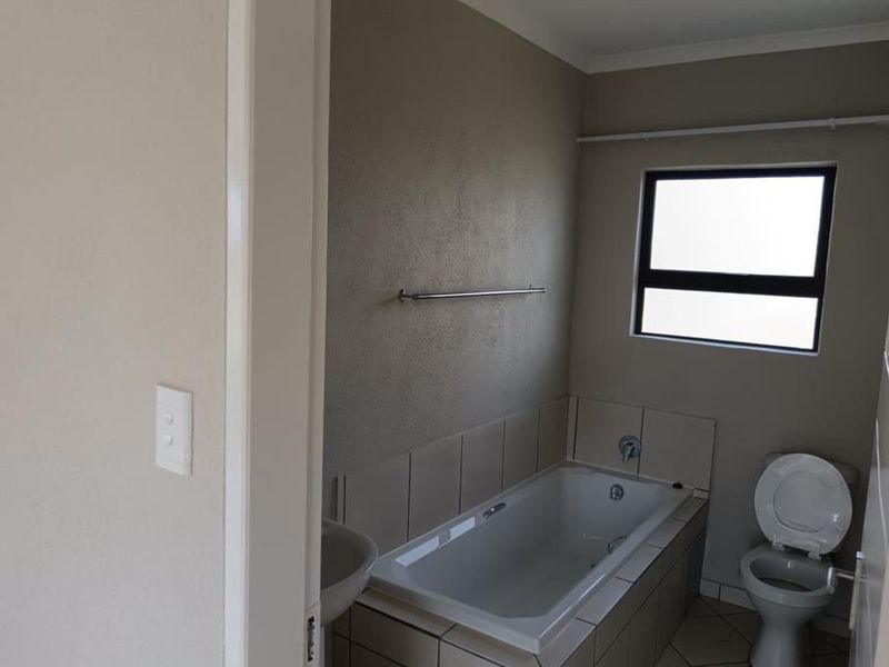A functional bathroom featuring a built-in bathtub with tiled surround, a toilet, and a towel rail, finished with neutral wall tones.