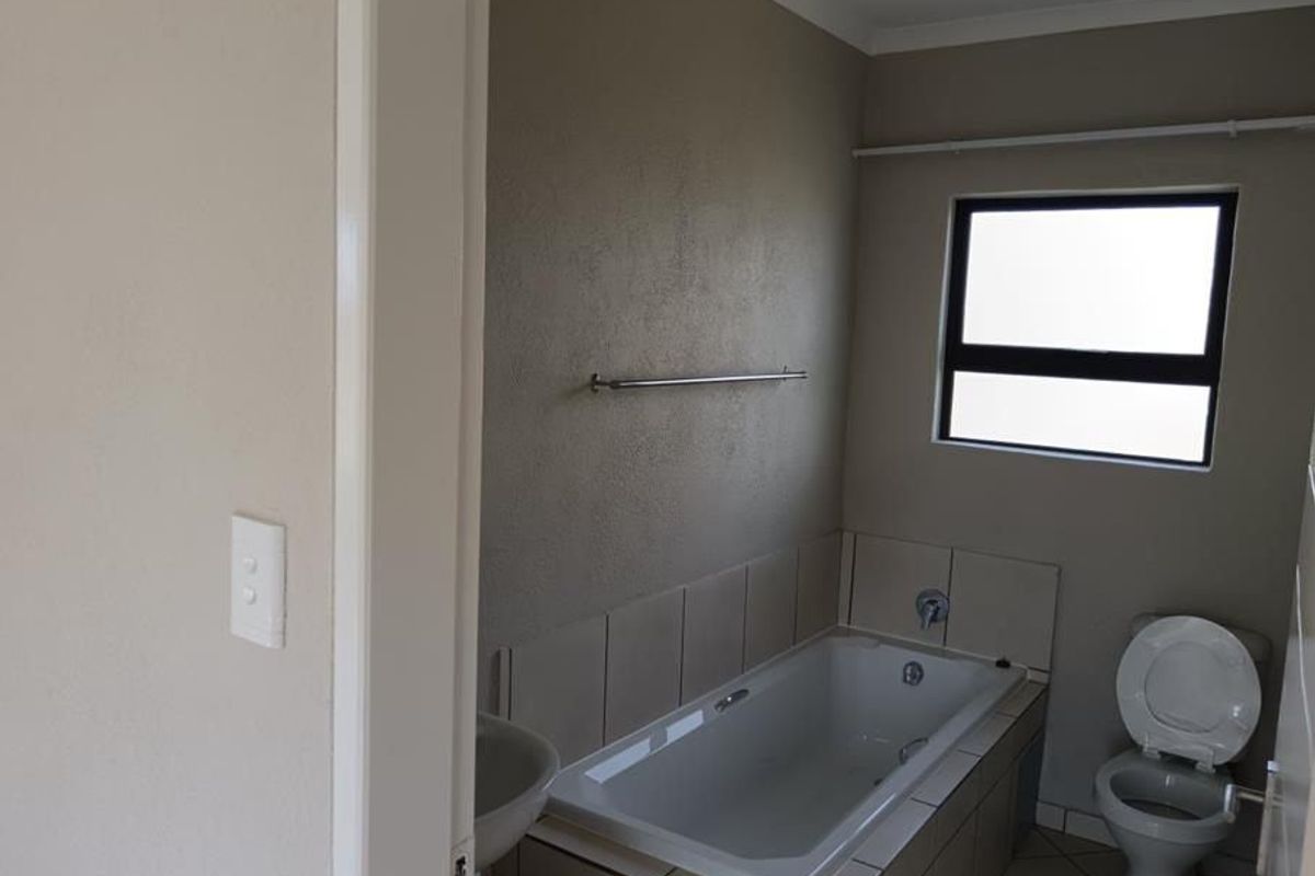A functional bathroom featuring a built-in bathtub with tiled surround, a toilet, and a towel rail, finished with neutral wall tones.
