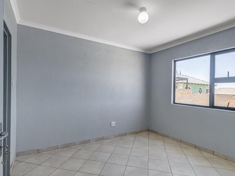 A clean, empty bedroom featuring neutral grey walls, tiled flooring, and an aluminium-framed window, providing a versatile space ready for personalization.