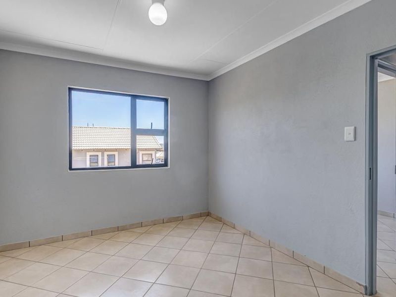 A clean, empty bedroom featuring neutral grey walls, tiled flooring, and an aluminium-framed window, providing a versatile space ready for personalization.