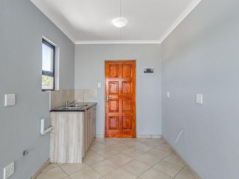 A functional scullery or utility area featuring built-in cabinetry, a stainless steel sink, tiled flooring, and a solid timber door.