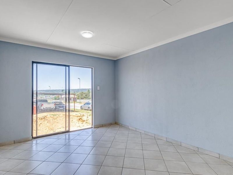 An empty living room featuring light blue walls, tiled flooring, and a sliding glass door providing natural light and outdoor access.