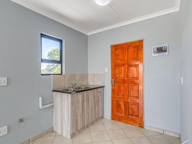 A clean, functional scullery area featuring built-in cabinetry, a stainless steel sink, tiled flooring, and a solid timber door.
