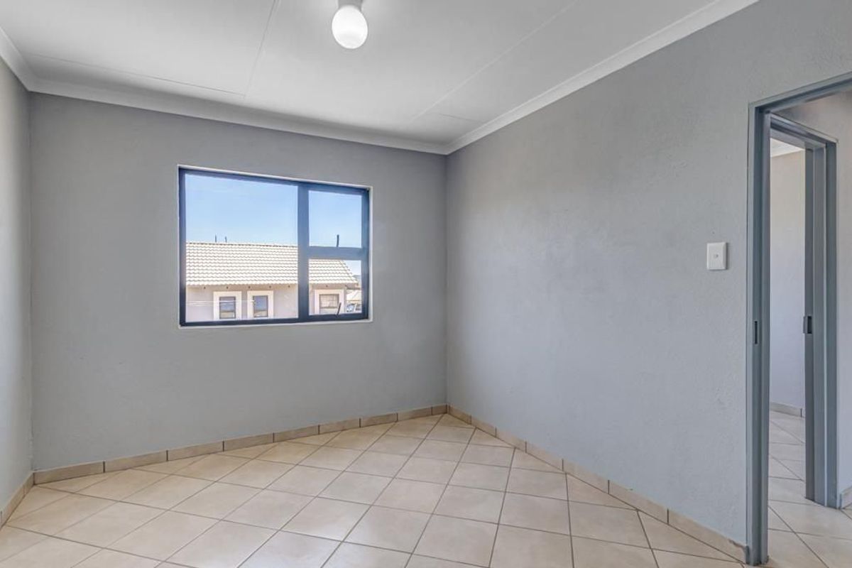A clean, empty bedroom featuring neutral grey walls, tiled flooring, and an aluminium-framed window, offering a blank canvas for personalization.