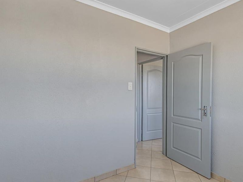 A clean, empty hallway featuring neutral grey walls, tiled flooring, and panelled interior doors leading to adjacent rooms.
