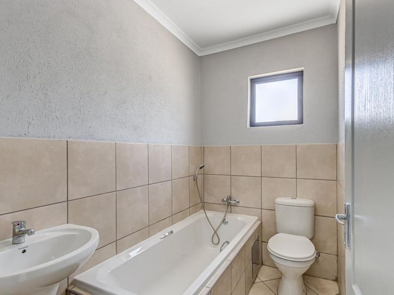 A clean, functional bathroom featuring a bathtub with handheld shower, pedestal basin, and toilet, finished with neutral wall and floor tiling.