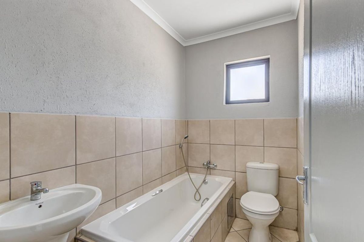 A clean, functional bathroom featuring a bathtub with handheld shower, pedestal basin, and toilet, finished with neutral wall and floor tiling.