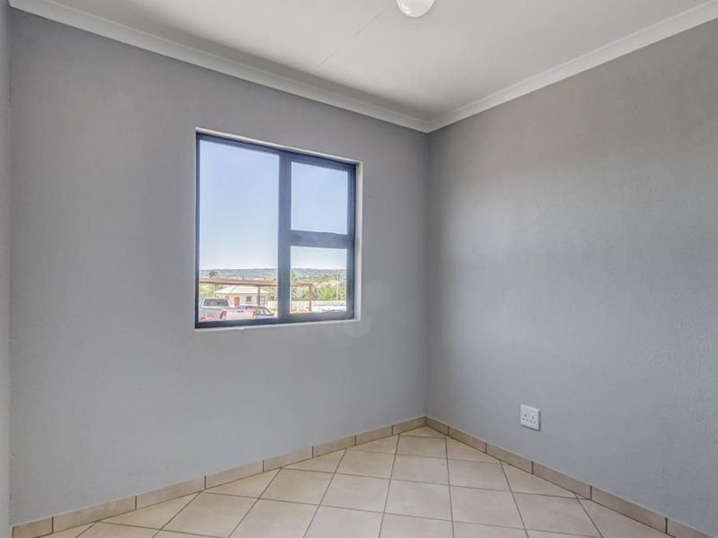 A clean, empty bedroom featuring neutral grey walls, tiled flooring, and an aluminium-framed window providing natural light.