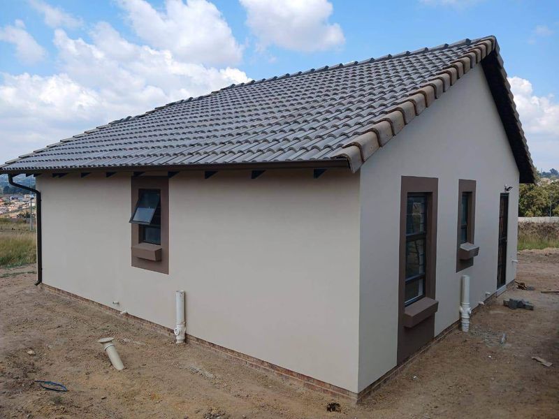 Rear exterior view of a modern house featuring a tiled roof, aluminium window frames, and exposed plumbing pipes on a newly constructed property.