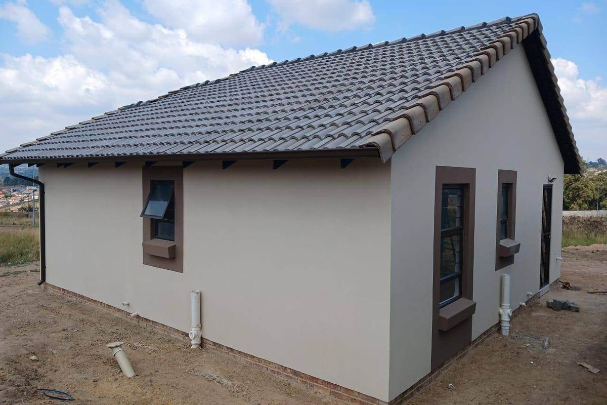 Rear exterior view of a modern house featuring a tiled roof, aluminium window frames, and exposed plumbing pipes on a newly constructed property.