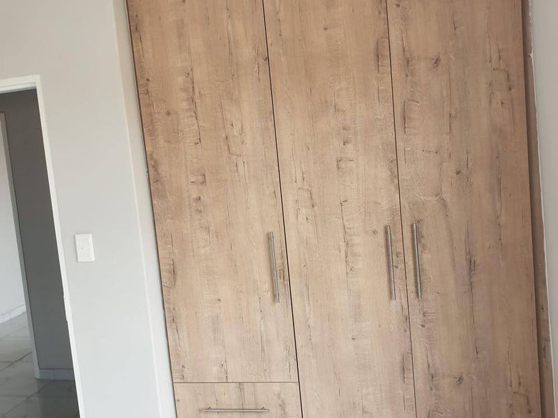A clean, modern bedroom featuring light wood-grain built-in wardrobes and polished white marble-look floor tiles.