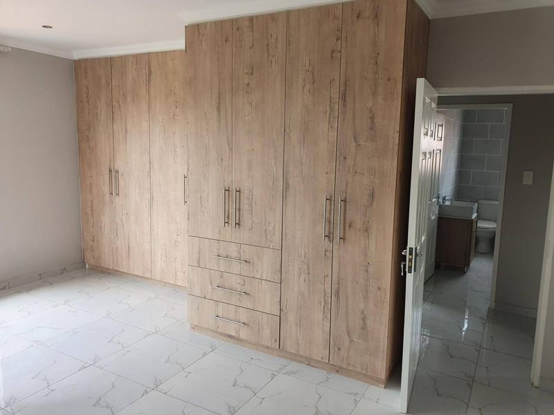 Spacious bedroom featuring modern wood-finish built-in cupboards, sleek marble-look tiled flooring, and direct access to an en-suite bathroom.