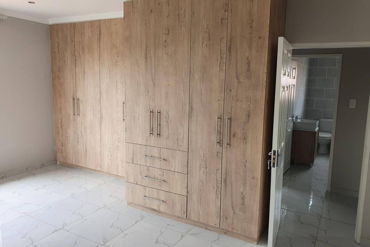 Spacious bedroom featuring modern wood-finish built-in cupboards, sleek marble-look tiled flooring, and direct access to an en-suite bathroom.