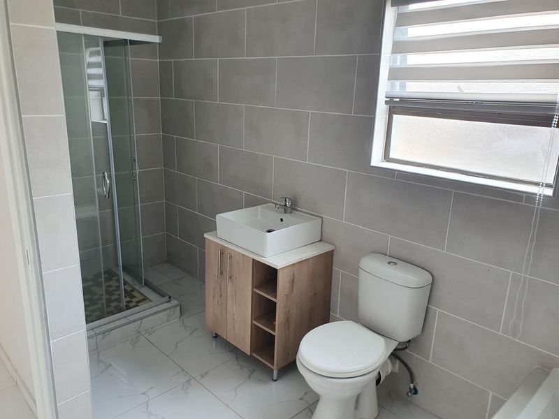 A modern bathroom featuring a glass shower enclosure, a wood-finish vanity with a vessel sink, and neutral wall and floor tiling.