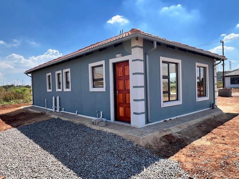 A modern single-story house exterior featuring grey rendered walls, white trim detailing, a tiled roof, and a timber entrance door with paved surrounds.