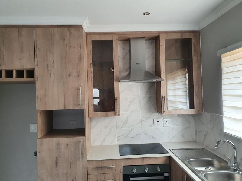 Modern kitchen featuring wood-look cabinetry, marble-effect tiled backsplash, integrated stainless steel appliances, and a double bowl sink with a contemporary mixer tap.