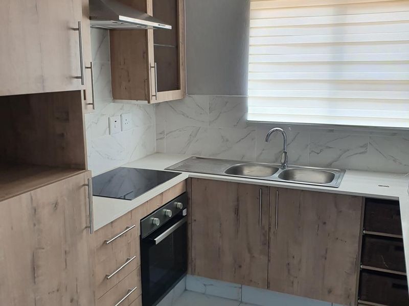 Modern kitchen featuring wood-look cabinetry, marble-effect tiled flooring and backsplash, integrated electric hob, oven, and stainless steel sink with contemporary finishes.