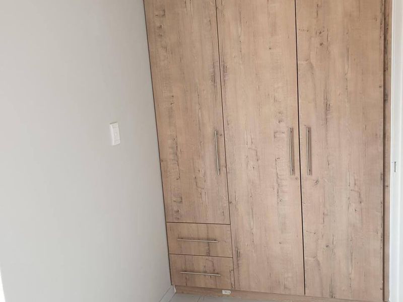 A clean bedroom interior featuring modern wood-finish built-in wardrobes and light-colored marble-effect floor tiles.