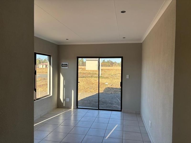 A bright, empty living area featuring neutral tiled flooring, recessed lighting, and a sliding glass door providing access to the exterior.