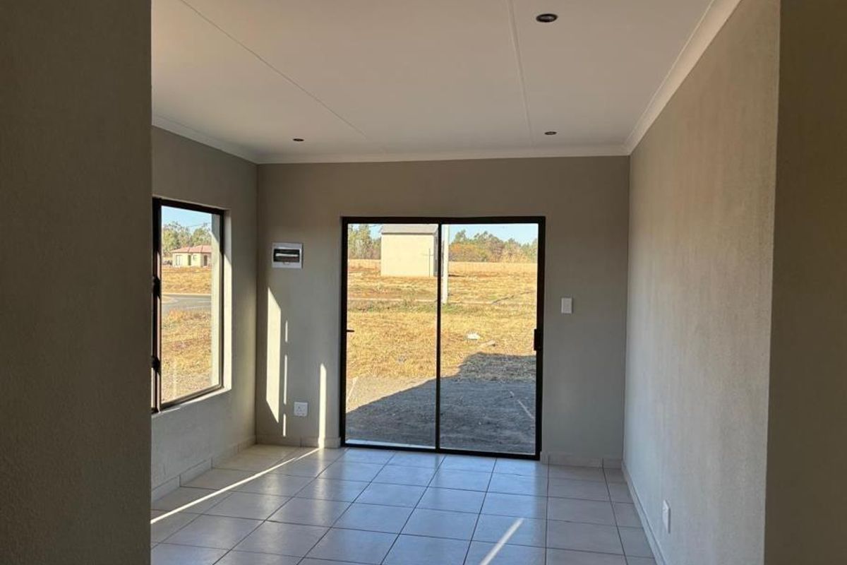 A bright, empty living area featuring neutral tiled flooring, recessed lighting, and a sliding glass door providing access to the exterior.