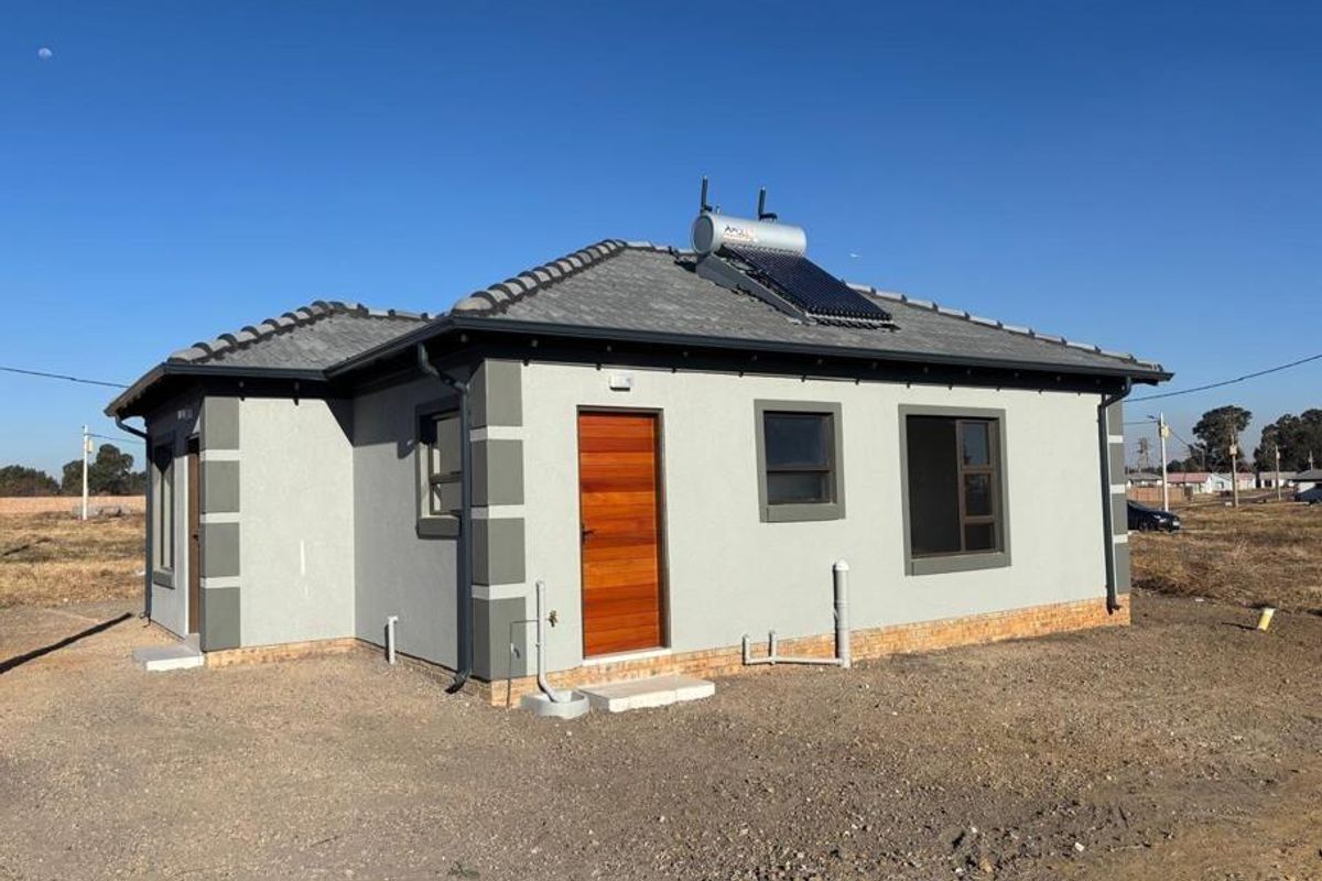 Rear view of a modern single-story house featuring a tiled roof, solar water heating system, timber door, and aluminium window frames.
