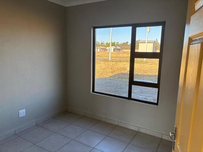 A clean, empty bedroom featuring neutral wall paint, tiled flooring, and a large window providing natural light and exterior views.