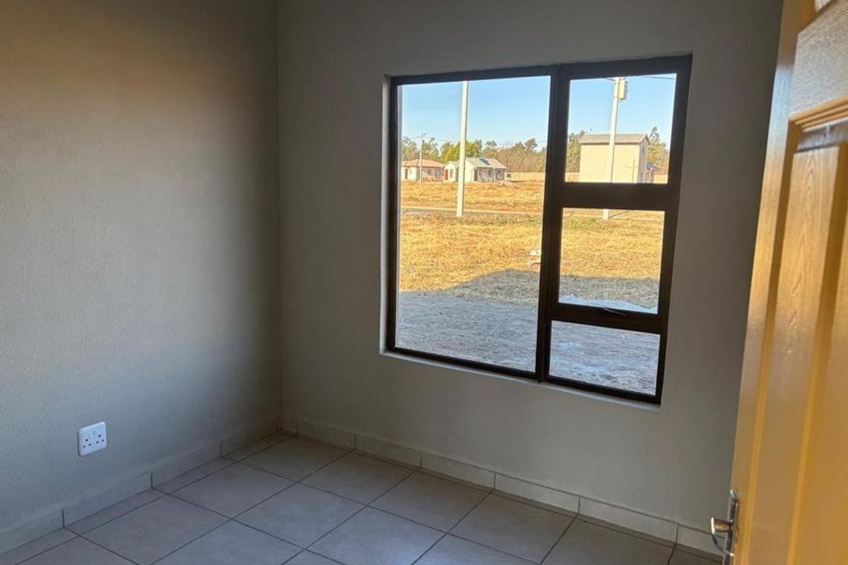 A clean, empty bedroom featuring neutral wall paint, tiled flooring, and a large window providing natural light and exterior views.
